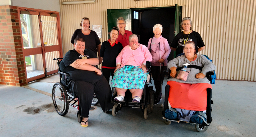 Men and women living with disabilities standing in a group photo smiling