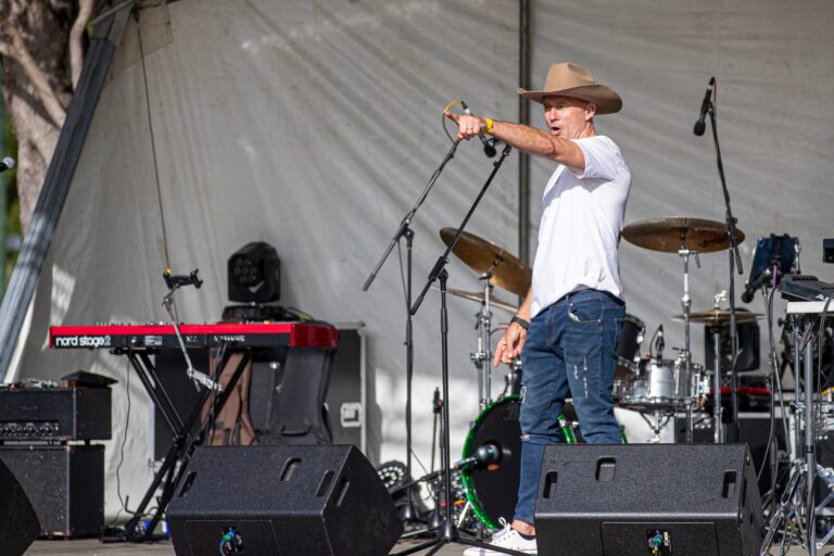 A man in a white shirt and cowboy hat performs on stage