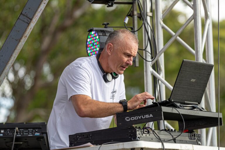 A DJ wearing a white shirt operates a mixing desk
