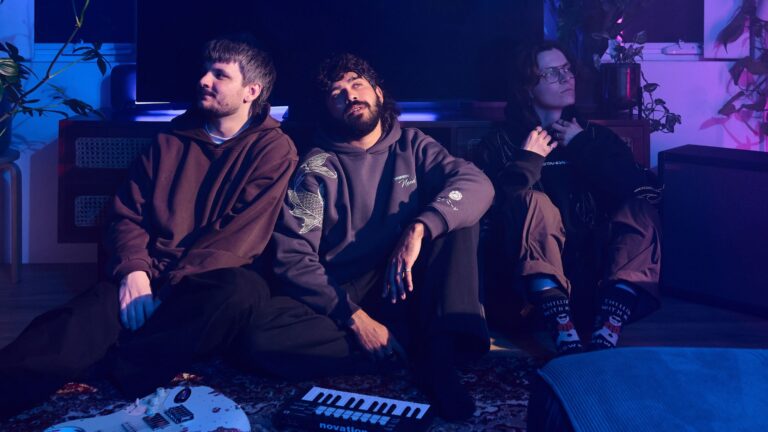 The three members of band Sophian sitting in a darkened room in front of a keyboard and electric guitar