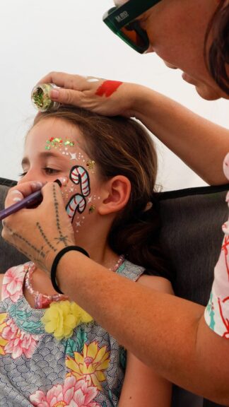 A face painter paints floral designs on a child's face